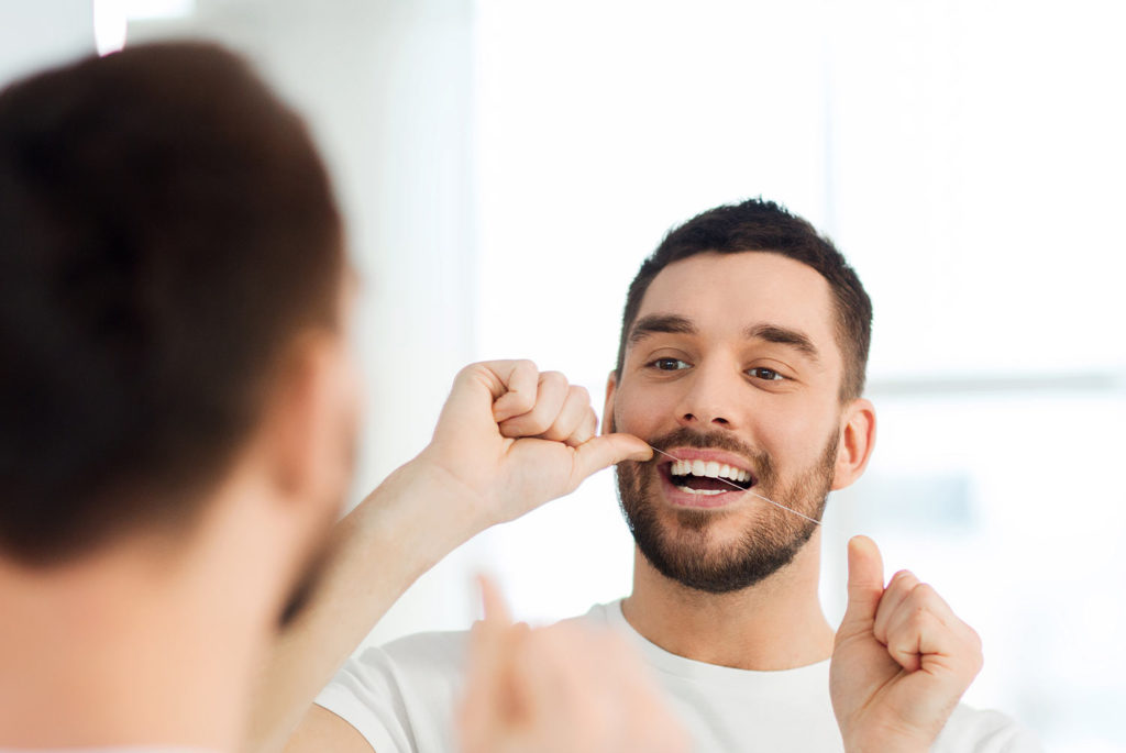 Man looking in the mirror while he flosses his teeth